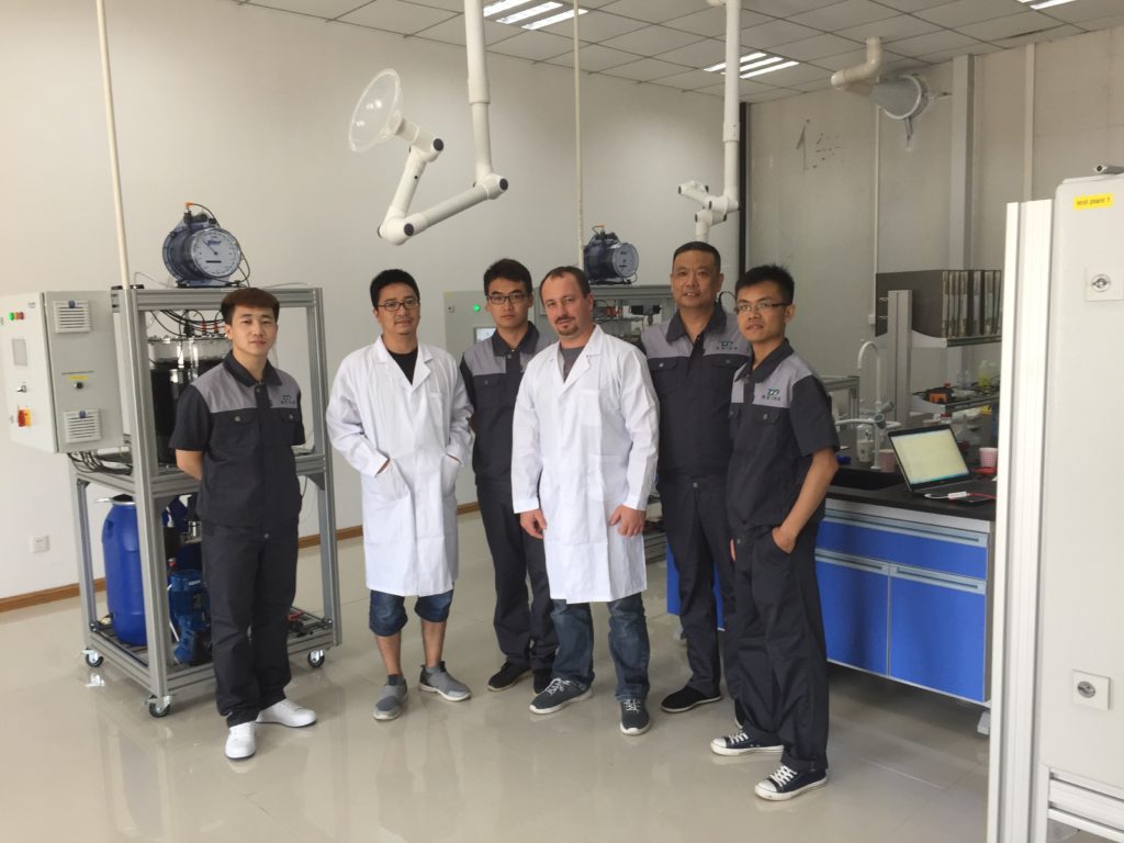 fünf chinesische Männer und der Chief Technology von der FlexBio Technologie GmbH in Arbeitskleidung, die vor den Versuchsanlagen der FelxBio Technologie GmbH in einem Labor in China stehen