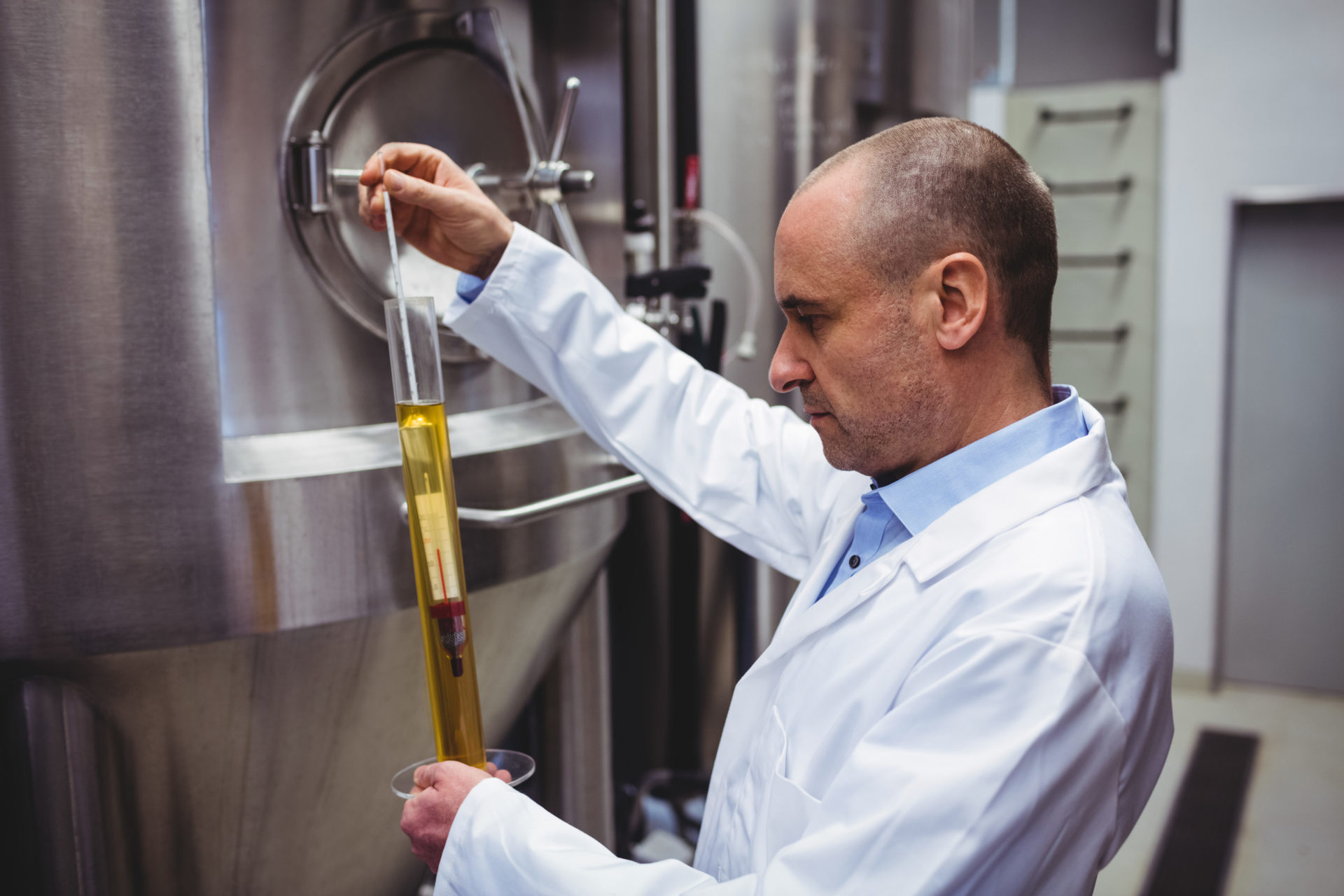 Abwassertechnik, ein Mitarbeiter in einem weißen Kittel, der die Qualität des Beers mithilfe eines Thermometers in einer Brauerei überprüft